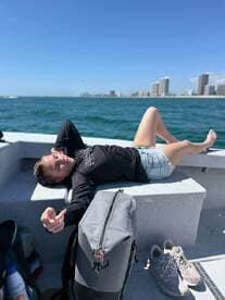A young woman relaxing on the boat's seating area, enjoying a sunny day on the water with a city skyline in the background.
