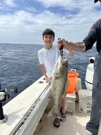 A young angler proudly displaying a large Grouper while fishing on a boat, showcasing a successful day on the water.