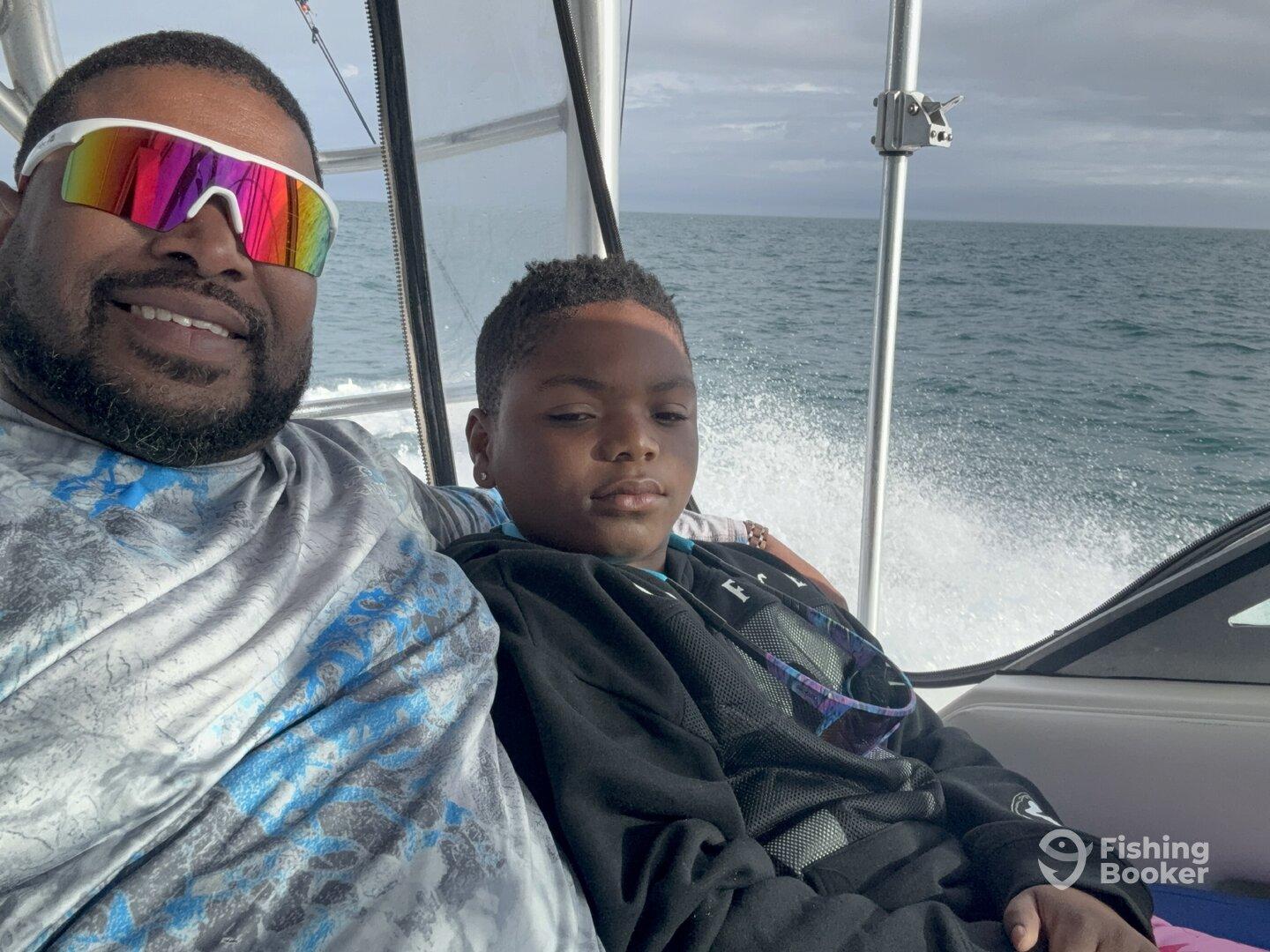 A father and son enjoying a fishing trip on a boat, showcasing a relaxed moment while cruising on the water.