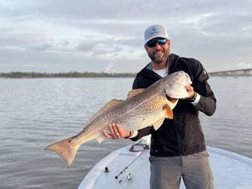 Angler proudly displaying a large Redfish while fishing on a calm waterway.