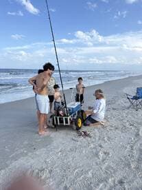 A group of young anglers engaged in fishing activities on the beach, with a cooler and fishing gear visible, showcasing a fun day by the ocean.