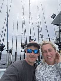 A couple enjoying a fishing trip on a boat, surrounded by fishing rods, capturing a moment together.