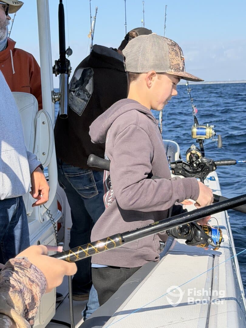 A young angler focused on reeling in a catch while fishing on a boat, surrounded by fellow anglers on a sunny day.