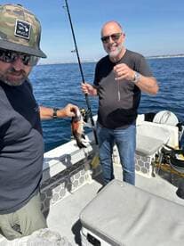 Two anglers enjoying a fishing trip, one holding a freshly caught fish while the other prepares their line on a boat.