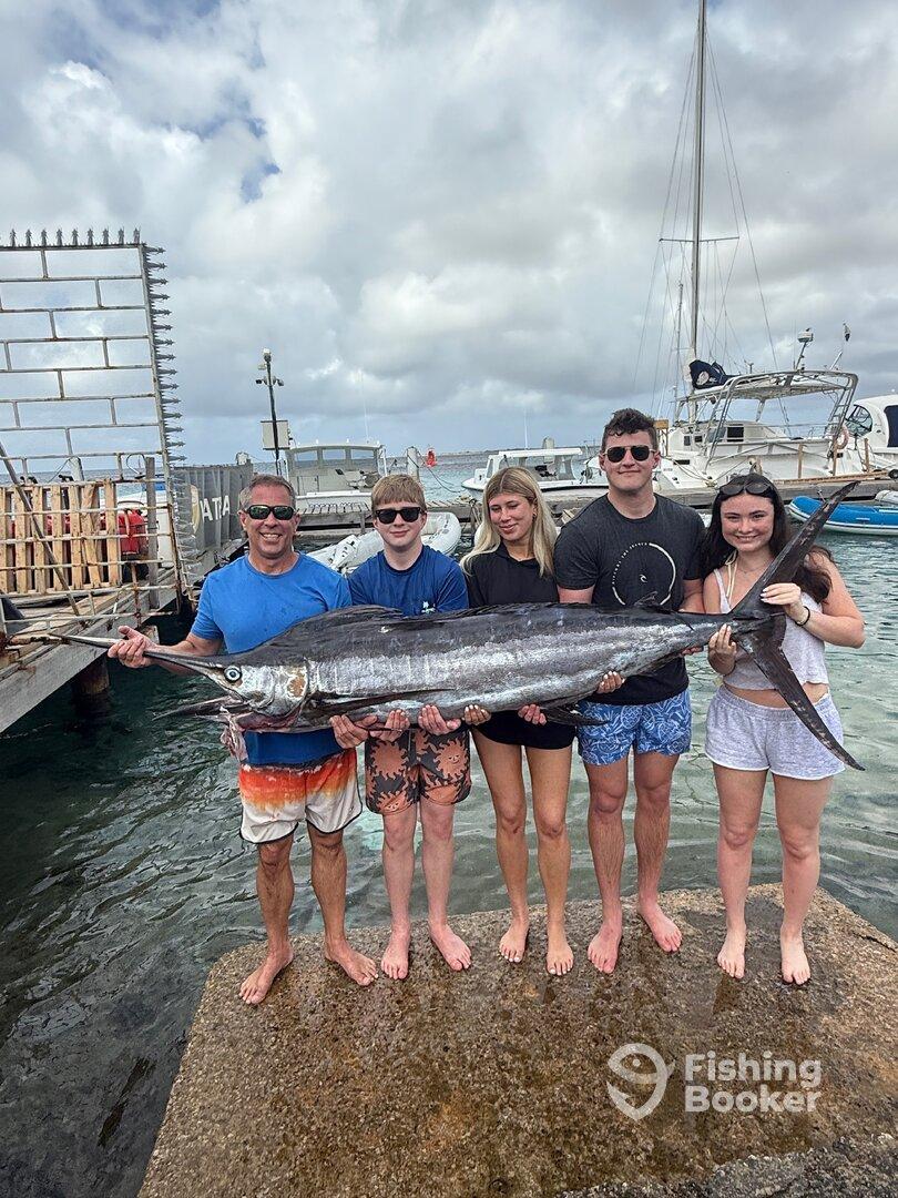 A family proudly displays a large Marlin at the dock after a successful fishing trip.