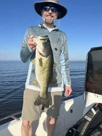 Angler proudly displaying a large Largemouth Bass while fishing on a sunny day.