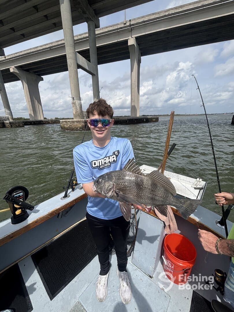 A young angler proudly displaying a large Black Drum while fishing under a bridge, showcasing a successful day on the water.