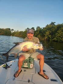 Angler proudly displaying a large Tarpon while fishing in a scenic mangrove area.