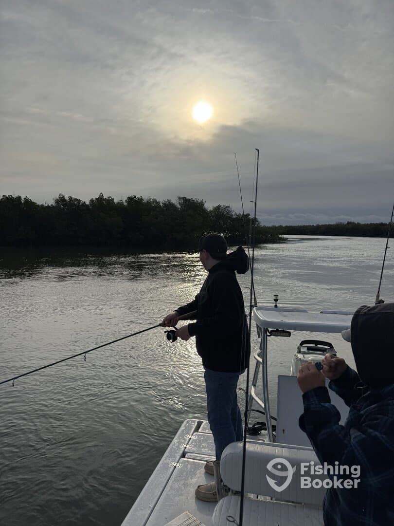 Two anglers casting lines from a boat during a serene fishing trip at sunset, surrounded by lush mangroves.