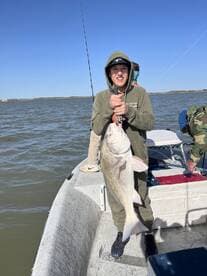 A young angler proudly displaying a large Redfish while fishing on a boat in calm waters.
