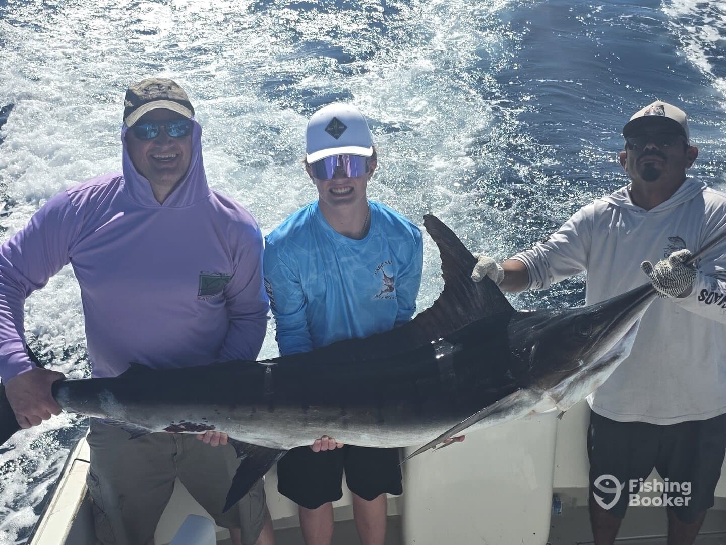 Three anglers proudly displaying a large Swordfish aboard a fishing charter in open waters.