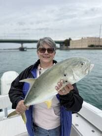 A proud angler holding a large Yellowtail at a scenic fishing spot, showcasing a successful day on the water.