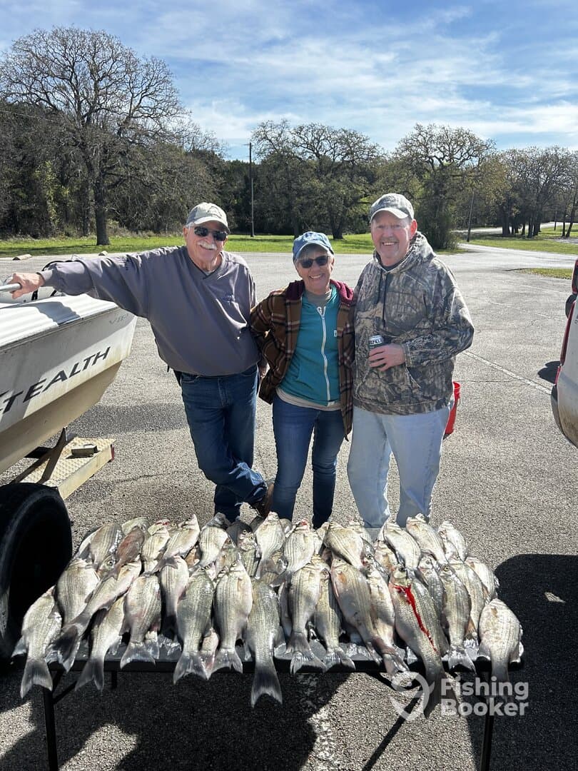 A group of three anglers proudly posing with their catch of striped bass displayed on a table after a successful fishing trip.