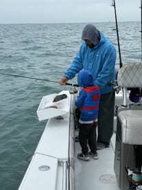 A young boy in a life jacket watches attentively as an adult prepares to cast a fishing line from the boat, showcasing a bonding moment on the water.