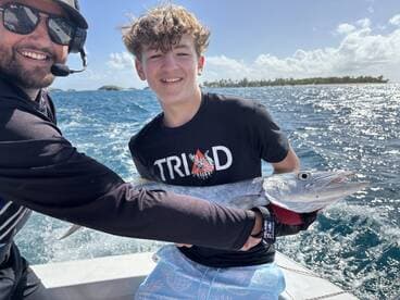 A young angler proudly holding a large Barracuda while enjoying a fishing trip on a sunny day.