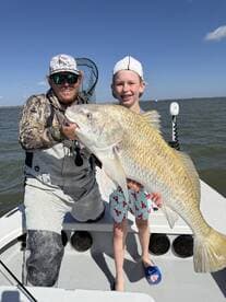 A young angler proudly displaying a large Redfish while fishing on a boat, showcasing a memorable moment on the water.