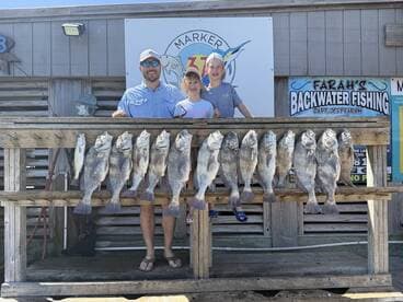 A proud family showcases their catch of the day, featuring several large fish displayed on a catch board at a fishing charter location.