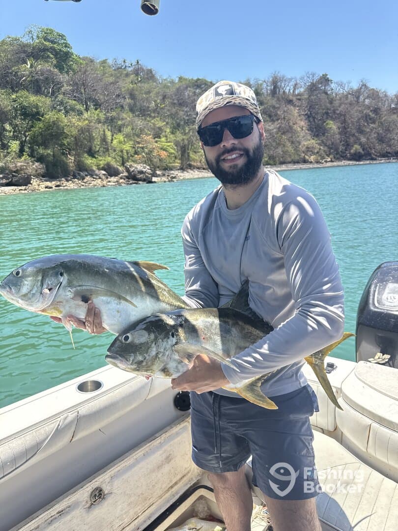 Angler proudly displaying two large Yellowtail fish while on a boat in a scenic fishing location.