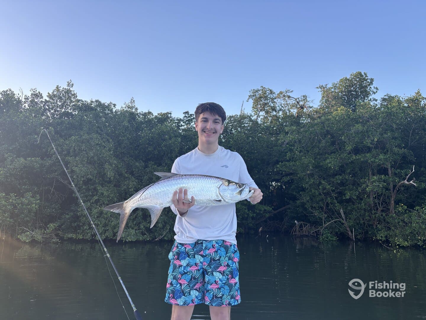 A young angler proudly displaying a large Tarpon while fishing in a scenic mangrove setting.