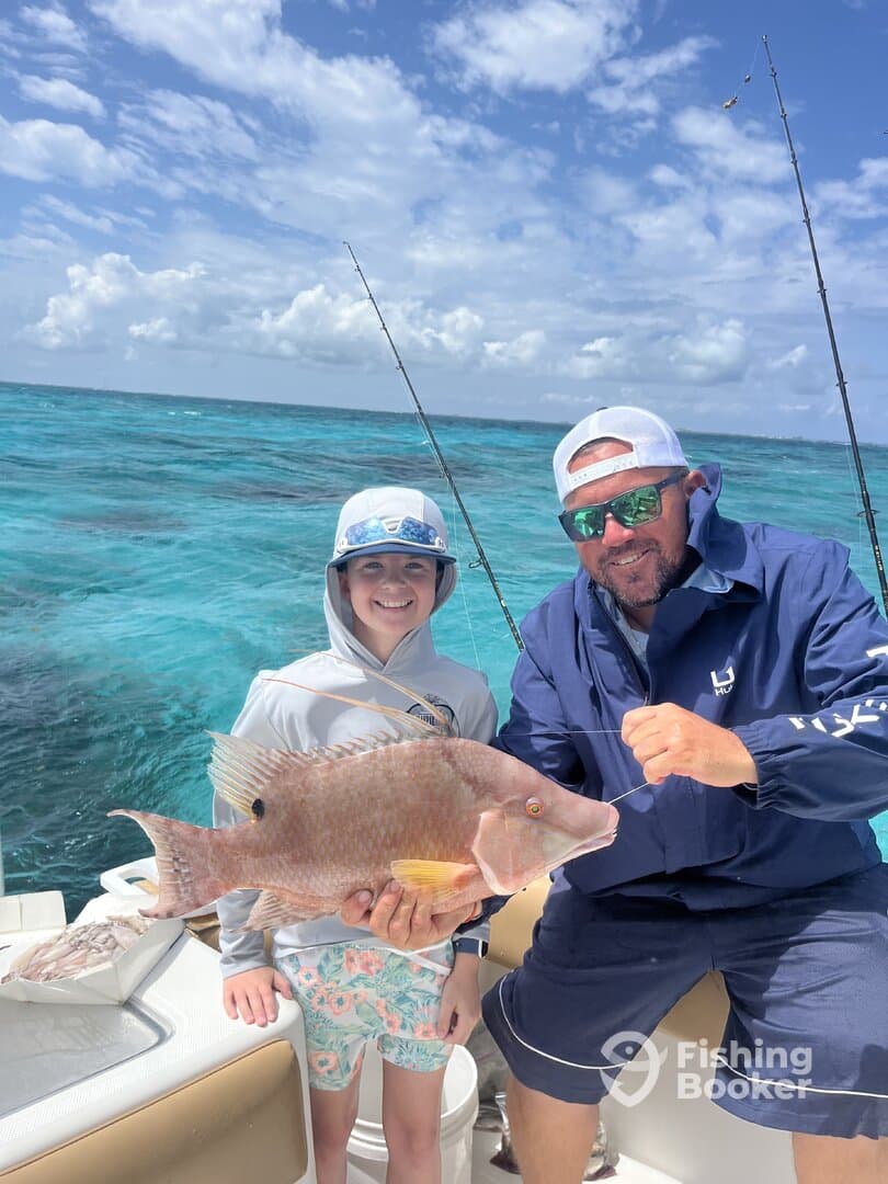 A young angler and an adult proudly displaying a large Snapper while fishing in clear blue waters.