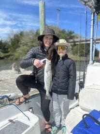 A proud mother and her child display a large Speckled Trout while fishing from a boat, showcasing a fun family fishing experience.