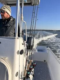 A fisherman at the helm of a center console boat, navigating through calm waters with fishing rods ready for action.