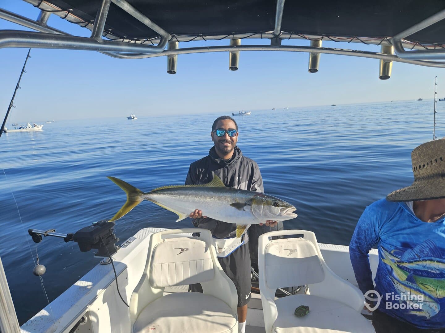 Angler proudly displaying a large Yellowtail while fishing on a calm day at sea, with other boats visible in the background.