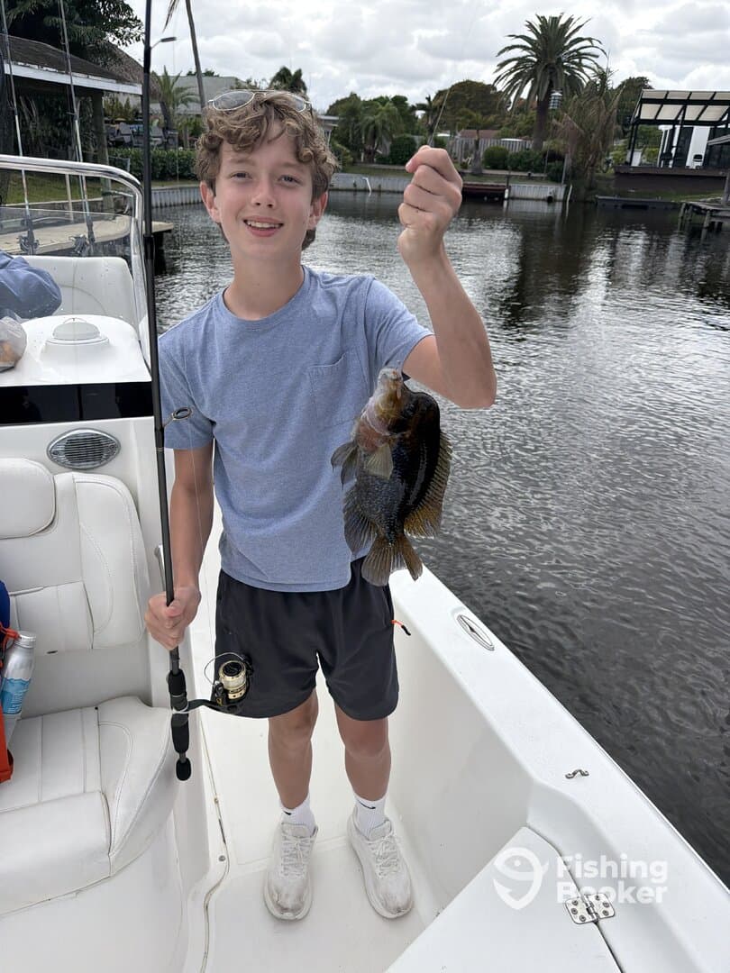 A young angler proudly displaying a colorful fish while fishing from a boat in a scenic waterway.
