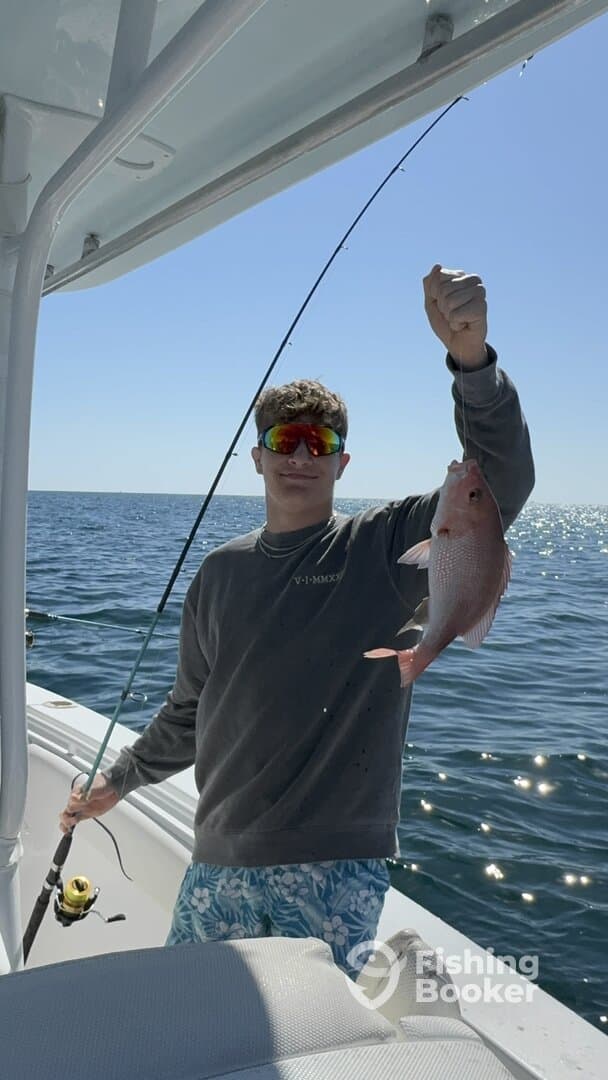 A young angler proudly displaying a Snapper while fishing on a sunny day.