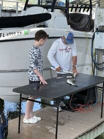 A young boy and an adult are preparing fish on a cleaning table at the dock, showcasing their catch after a fishing trip.