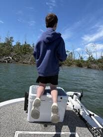 A young angler standing on a cooler, casting a line while fishing in a scenic waterway surrounded by mangroves.
