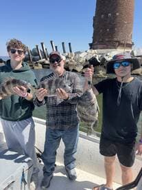 A family group proudly displaying their catch of Black Drum while fishing near a coastal lighthouse.