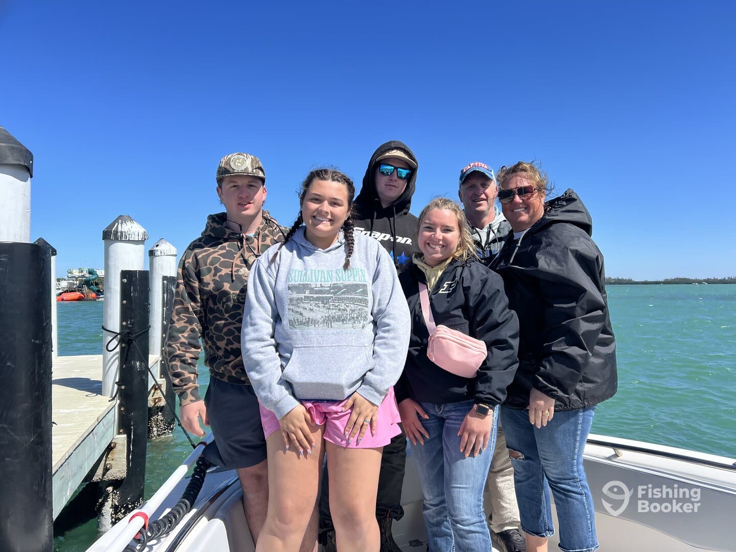 A group of six individuals posing on a boat at the dock, enjoying a sunny day on the water.