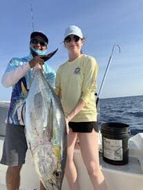 Two anglers proudly displaying a large Yellowfin Tuna on a fishing charter in open waters.