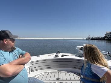 A man and a young girl enjoying a day on a boat, gazing at the serene waters and sandy shorelines, highlighting a family fishing experience.