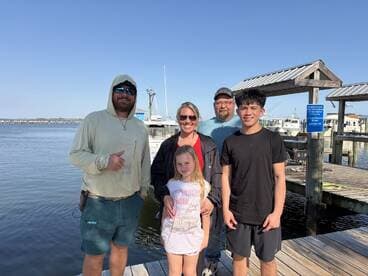 A family poses together at the dock, celebrating their fishing trip with smiles and a scenic waterfront backdrop.