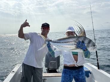 Two anglers proudly displaying a large Roosterfish while fishing offshore, showcasing a successful day on the water.