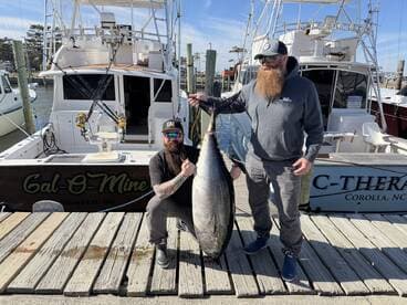 Two anglers proudly displaying a large Bluefin Tuna on the dock next to their boat, Gal-O-Mine, after a successful fishing trip in Manteo, NC.