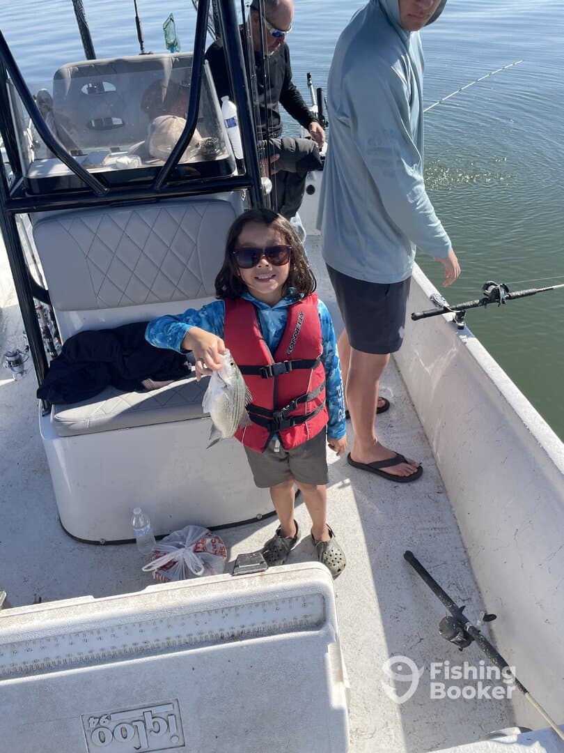 A young angler proudly displaying a caught fish while fishing on a boat, showcasing a family-friendly fishing experience.
