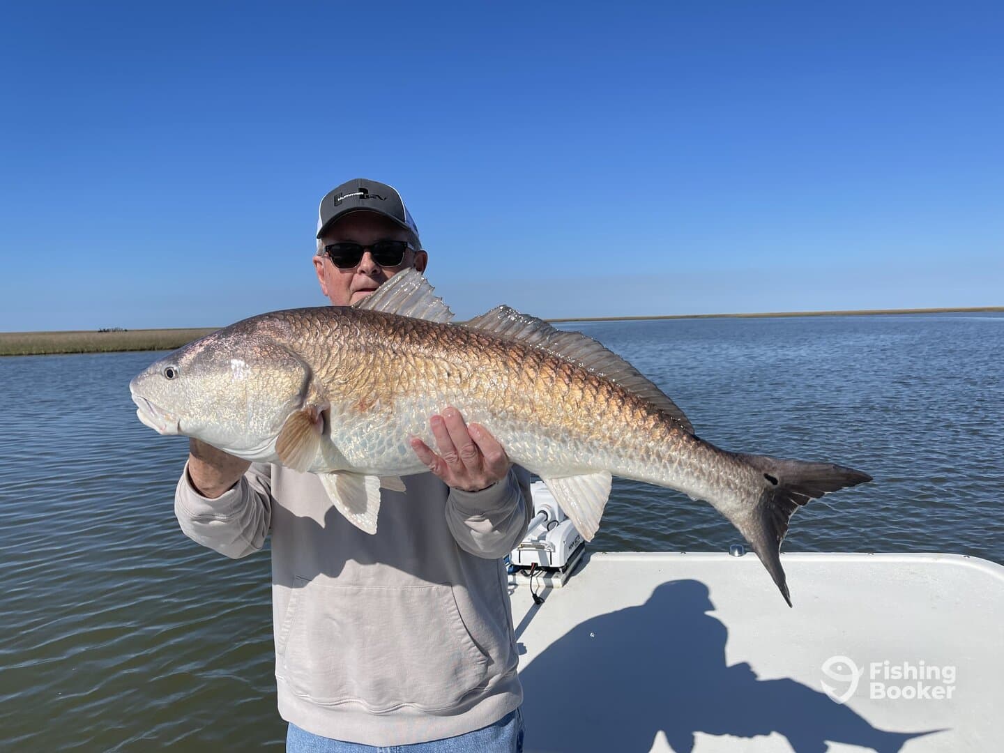 An angler proudly displaying a large Redfish while fishing in a scenic coastal environment.