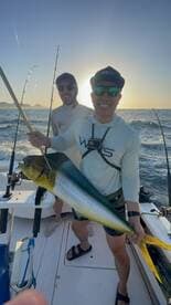 Two anglers proudly displaying a large Mahi Mahi while fishing in the ocean during sunset.