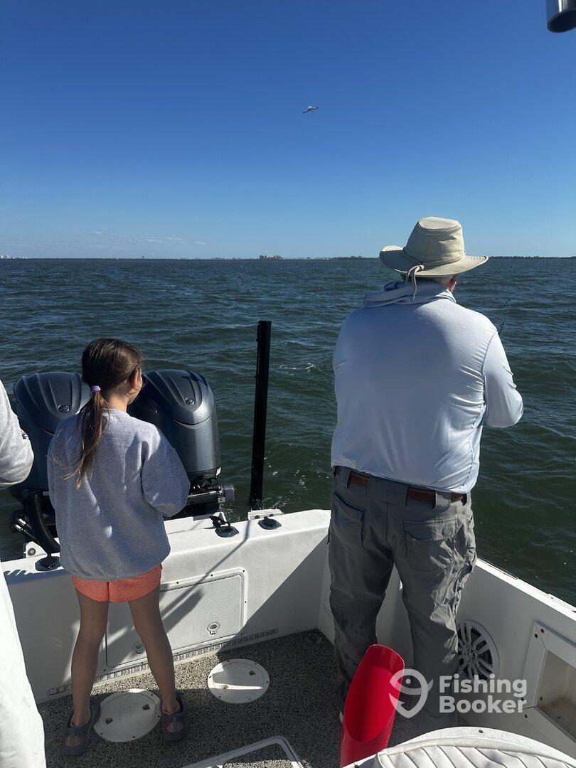 A young girl and an adult are fishing from a boat, enjoying a sunny day on the water.