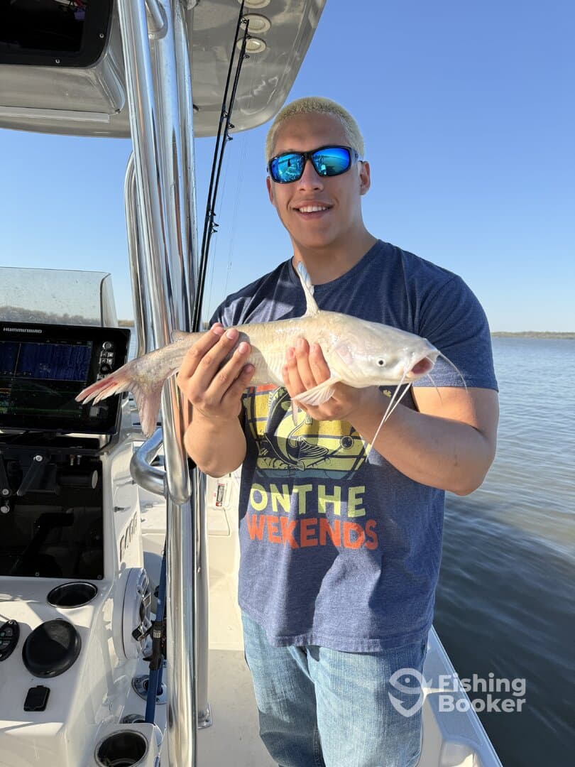 A young angler proudly displaying a freshly caught catfish while on a fishing trip, with a scenic water backdrop.