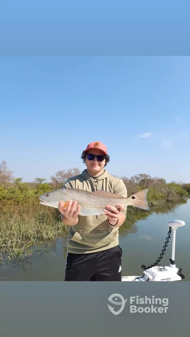 Angler proudly displaying a Redfish while fishing in a scenic coastal environment.