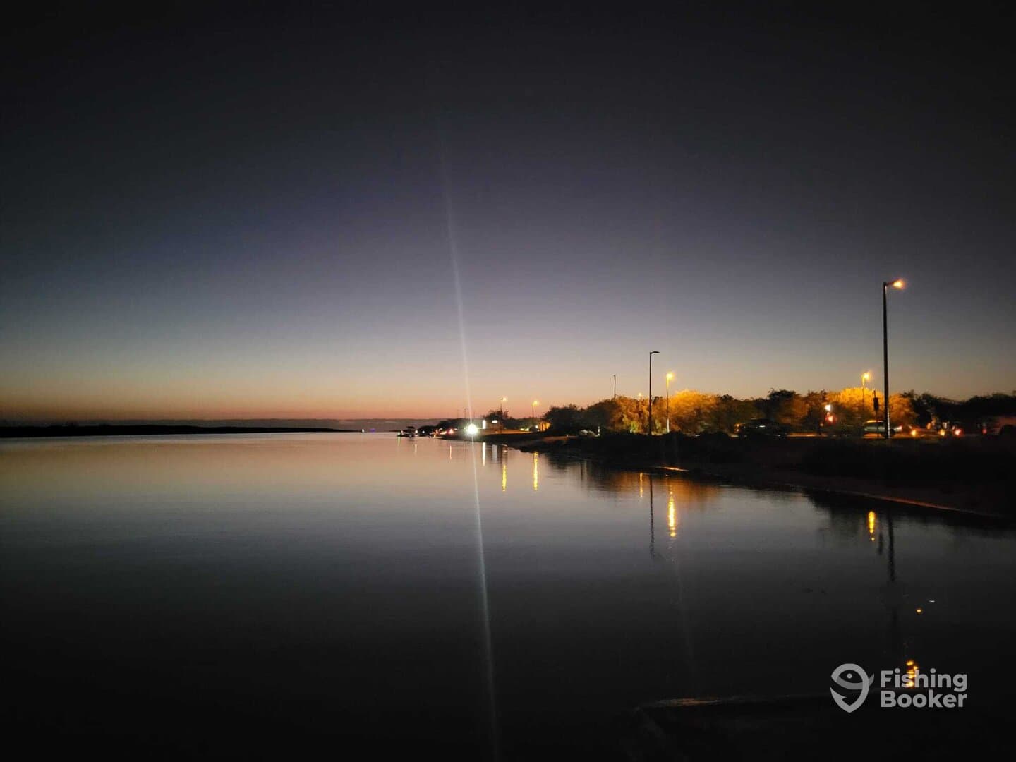 A serene evening view of the water reflecting the twilight sky, with lights from the shore illuminating the scene.