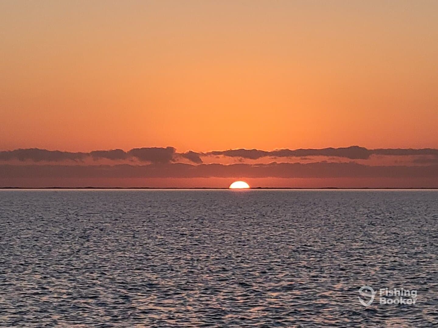 A serene sunset over the ocean, casting warm hues across the water, creating a tranquil fishing atmosphere.