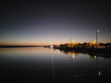 A serene evening view of the water reflecting the twilight sky, with lights from the shore illuminating the scene.