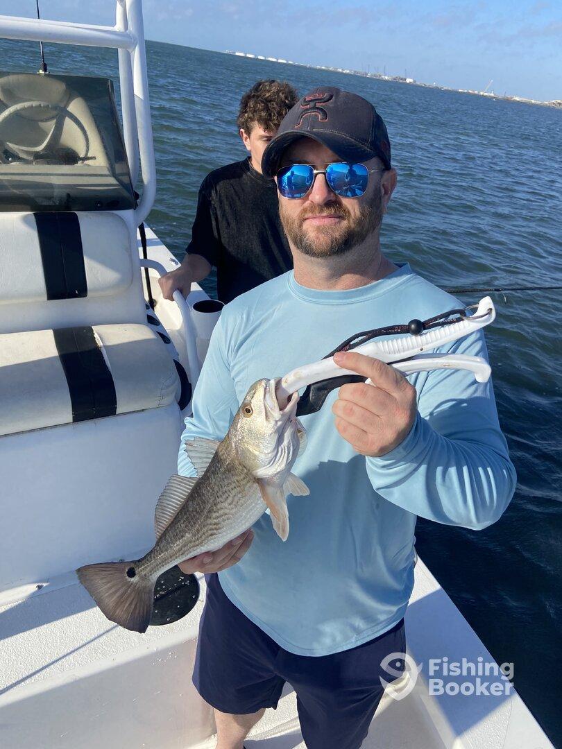 Angler proudly displaying a striped bass while fishing on a boat, with a scenic water backdrop.