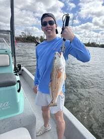 Angler proudly displaying a large Redfish while fishing from a boat, showcasing a successful day on the water.