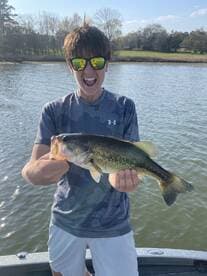 A young angler excitedly holds up a large Largemouth Bass while fishing on a serene lake.